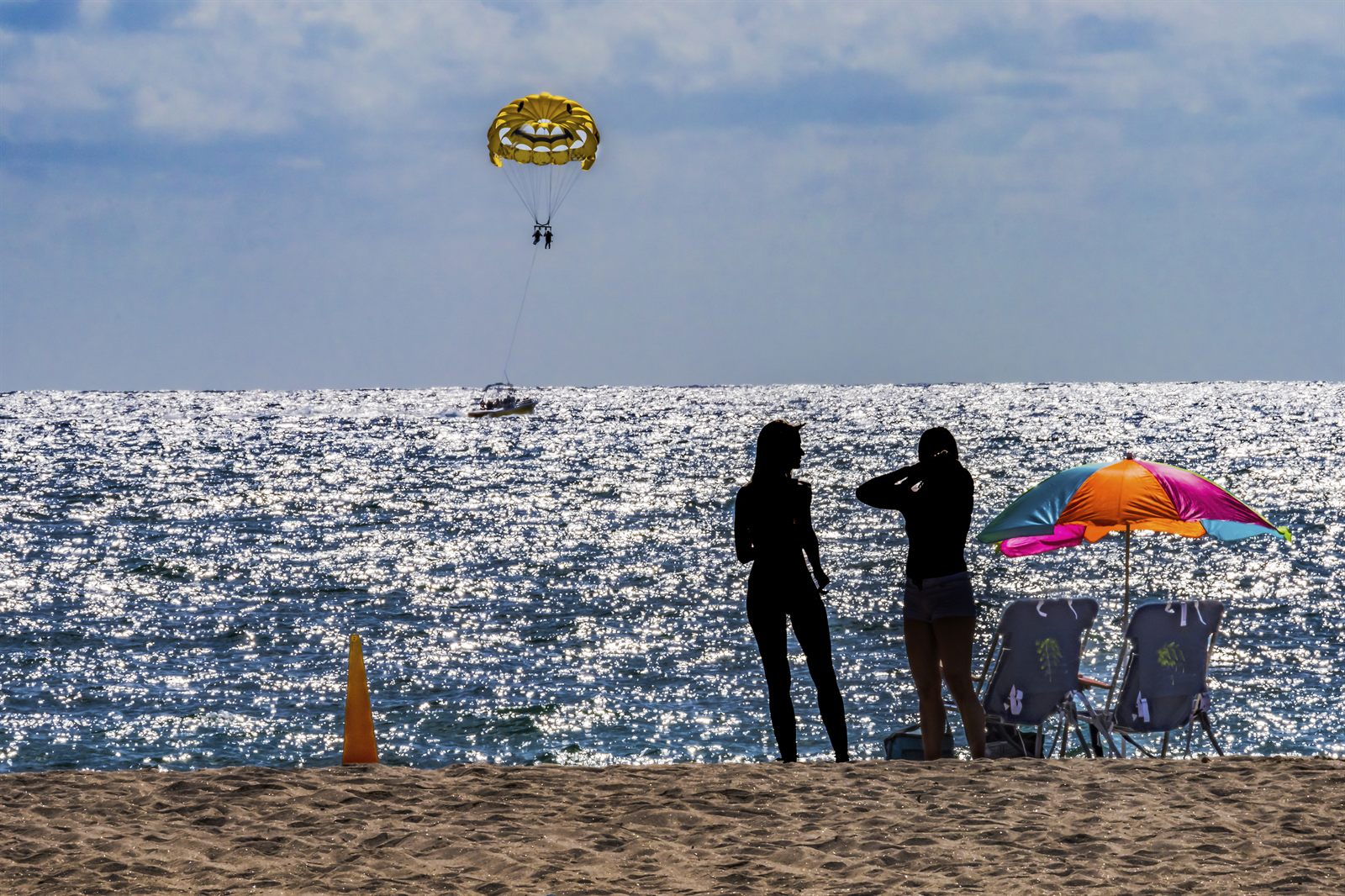 Two friends on a Fort Lauderdale beach at sunset with a parasail over the sea